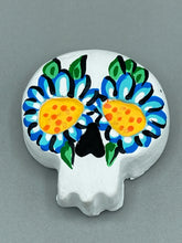 Load image into Gallery viewer, Heal emotionally and spiritually through art by honoring a loved one with a unique and beautiful Purple Spirit Piece Memorial Skull Art. Day Of The Dead Spirit Piece is an ideal addition to your ofrenda or altar that will provide a lasting tribute. These handcrafted polymer clay skull figurines are adorned with hand-painted light blue floral designs for the eyes. H 1 1/2” x W 1 1/2” x D 3/4”