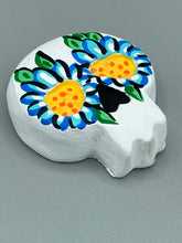 Load image into Gallery viewer, Heal emotionally and spiritually through art by honoring a loved one with a unique and beautiful Purple Spirit Piece Memorial Skull Art. Day Of The Dead Spirit Piece is an ideal addition to your ofrenda or altar that will provide a lasting tribute. These handcrafted polymer clay skull figurines are adorned with hand-painted light blue floral designs for the eyes. H 1 1/2” x W 1 1/2” x D 3/4”