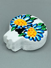 Load image into Gallery viewer, Heal emotionally and spiritually through art by honoring a loved one with a unique and beautiful Purple Spirit Piece Memorial Skull Art. Day Of The Dead Spirit Piece is an ideal addition to your ofrenda or altar that will provide a lasting tribute. These handcrafted polymer clay skull figurines are adorned with hand-painted light blue floral designs for the eyes. H 1 1/2” x W 1 1/2” x D 3/4”