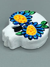 Load image into Gallery viewer, Heal emotionally and spiritually through art by honoring a loved one with a unique and beautiful Purple Spirit Piece Memorial Skull Art. Day Of The Dead Spirit Piece is an ideal addition to your ofrenda or altar that will provide a lasting tribute. These handcrafted polymer clay skull figurines are adorned with hand-painted dark blue floral designs for the eyes. H 1 1/2” x W 1 1/2” x D 3/4”