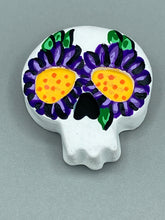 Load image into Gallery viewer, Heal emotionally and spiritually through art by honoring a loved one with a unique and beautiful Purple Spirit Piece Memorial Skull Art. Day Of The Dead Spirit Piece is an ideal addition to your ofrenda or altar that will provide a lasting tribute. These handcrafted polymer clay skull figurines are adorned with hand-painted dark purple floral designs for the eyes. H 1 1/2” x W 1 1/2” x D 3/4”