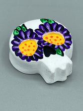 Load image into Gallery viewer, Heal emotionally and spiritually through art by honoring a loved one with a unique and beautiful Purple Spirit Piece Memorial Skull Art. Day Of The Dead Spirit Piece is an ideal addition to your ofrenda or altar that will provide a lasting tribute. These handcrafted polymer clay skull figurines are adorned with hand-painted dark purple floral designs for the eyes. H 1 1/2” x W 1 1/2” x D 3/4”