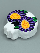 Load image into Gallery viewer, Heal emotionally and spiritually through art by honoring a loved one with a unique and beautiful Purple Spirit Piece Memorial Skull Art. Day Of The Dead Spirit Piece is an ideal addition to your ofrenda or altar that will provide a lasting tribute. These handcrafted polymer clay skull figurines are adorned with hand-painted dark purple floral designs for the eyes. H 1 1/2” x W 1 1/2” x D 3/4”