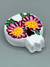 Load image into Gallery viewer, Heal emotionally and spiritually through art by honoring a loved one with a unique and beautiful Purple Spirit Piece Memorial Skull Art. Day Of The Dead Spirit Piece is an ideal addition to your ofrenda or altar that will provide a lasting tribute. These handcrafted polymer clay skull figurines are adorned with hand-painted pink floral designs for the eyes. H 1 1/2” x W 1 1/2” x D 3/4”