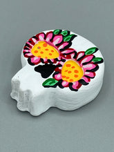 Load image into Gallery viewer, Heal emotionally and spiritually through art by honoring a loved one with a unique and beautiful Purple Spirit Piece Memorial Skull Art. Day Of The Dead Spirit Piece is an ideal addition to your ofrenda or altar that will provide a lasting tribute. These handcrafted polymer clay skull figurines are adorned with hand-painted pink floral designs for the eyes. H 1 1/2” x W 1 1/2” x D 3/4”