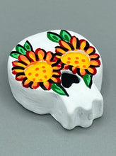 Load image into Gallery viewer, Heal emotionally and spiritually through art by honoring a loved one with a unique and beautiful Purple Spirit Piece Memorial Skull Art. Day Of The Dead Spirit Piece is an ideal addition to your ofrenda or altar that will provide a lasting tribute. These handcrafted polymer clay skull figurines are adorned with hand-painted bright orange floral designs for the eyes. H 1 1/2” x W 1 1/2” x D 3/4”