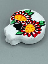 Load image into Gallery viewer, Heal emotionally and spiritually through art by honoring a loved one with a unique and beautiful Purple Spirit Piece Memorial Skull Art. Day Of The Dead Spirit Piece is an ideal addition to your ofrenda or altar that will provide a lasting tribute. These handcrafted polymer clay skull figurines are adorned with hand-painted red floral designs for the eyes. H 1 1/2” x W 1 1/2” x D 3/4”