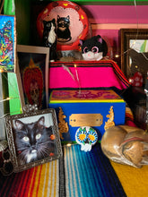 Load image into Gallery viewer, Heal emotionally and spiritually through art by honoring a loved one with a unique and beautiful Purple Spirit Piece Memorial Skull Art. Day Of The Dead Spirit Piece is an ideal addition to your ofrenda or altar that will provide a lasting tribute. These handcrafted polymer clay skull figurines are adorned with hand-painted dark floral designs for the eyes. H 1 1/2” x W 1 1/2” x D 3/4”