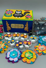 Load image into Gallery viewer, Heal emotionally and spiritually through art by honoring a loved one with a unique and beautiful Purple Spirit Piece Memorial Skull Art. Day Of The Dead Spirit Piece is an ideal addition to your ofrenda or altar that will provide a lasting tribute. These handcrafted polymer clay skull figurines are adorned with hand-painted dark floral designs for the eyes. H 1 1/2” x W 1 1/2” x D 3/4”