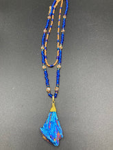 Load image into Gallery viewer, A bold deep blue kyanite wired stone pendant is surrounded by two strands of glass bead necklaces featuring a deep blue and gold shimmer palette. The shorter strand is designed to be worn as a collar or choker, while the longer second strand creates a striking contrast. With its bold appearance and eye-catching gemstone pendant, this necklace is a must-have for any jewelry collection. Necklace is 15” in length, can be adjusted to 18"