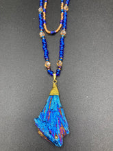 Load image into Gallery viewer, A bold deep blue kyanite wired stone pendant is surrounded by two strands of glass bead necklaces featuring a deep blue and gold shimmer palette. The shorter strand is designed to be worn as a collar or choker, while the longer second strand creates a striking contrast. With its bold appearance and eye-catching gemstone pendant, this necklace is a must-have for any jewelry collection. Necklace is 15” in length, can be adjusted to 18"