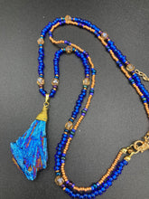 Load image into Gallery viewer, A bold deep blue kyanite wired stone pendant is surrounded by two strands of glass bead necklaces featuring a deep blue and gold shimmer palette. The shorter strand is designed to be worn as a collar or choker, while the longer second strand creates a striking contrast. With its bold appearance and eye-catching gemstone pendant, this necklace is a must-have for any jewelry collection. Necklace is 15” in length, can be adjusted to 18"