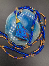 Load image into Gallery viewer, A bold deep blue kyanite wired stone pendant is surrounded by two strands of glass bead necklaces featuring a deep blue and gold shimmer palette. The shorter strand is designed to be worn as a collar or choker, while the longer second strand creates a striking contrast. With its bold appearance and eye-catching gemstone pendant, this necklace is a must-have for any jewelry collection. Necklace is 15” in length, can be adjusted to 18"