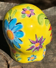 Load image into Gallery viewer, This ceramic skull statuette is a stunning piece of art inspired by nature. Its vibrant yellow hue is decorated with multi-color floral motifs, hearts, leaves and colorful accents, creating a beautiful piece of hand-painted, Day of the Dead-themed art. Measurements: H 2 3/4” x W 2” x D 2”