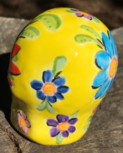 Load image into Gallery viewer, This ceramic skull statuette is a stunning piece of art inspired by nature. Its vibrant yellow hue is decorated with multi-color floral motifs, hearts, leaves and colorful accents, creating a beautiful piece of hand-painted, Day of the Dead-themed art. Measurements: H 2 3/4” x W 2” x D 2”