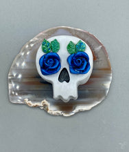 Load image into Gallery viewer, Cremation memorial art, such as Day of the Dead Spirit Pieces, provide a unique way to keep a loved one close to your heart. Handcrafted with care, each piece of artwork is specially tailored to the individual, providing a lasting reminder of those who are dearly missed. On altars and ofrendas, these pieces make a beautiful addition. Composed with meticulous attention to detail, these mini polymer clay skulls feature hand sculpted dark blue roses and leaves. H 1 1/2” x W 1 1/2” x D 3/4”