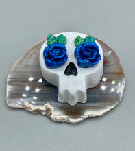 Load image into Gallery viewer, Cremation memorial art, such as Day of the Dead Spirit Pieces, provide a unique way to keep a loved one close to your heart. Handcrafted with care, each piece of artwork is specially tailored to the individual, providing a lasting reminder of those who are dearly missed. On altars and ofrendas, these pieces make a beautiful addition. Composed with meticulous attention to detail, these mini polymer clay skulls feature hand sculpted dark blue roses and leaves. H 1 1/2” x W 1 1/2” x D 3/4”