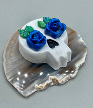 Load image into Gallery viewer, Cremation memorial art, such as Day of the Dead Spirit Pieces, provide a unique way to keep a loved one close to your heart. Handcrafted with care, each piece of artwork is specially tailored to the individual, providing a lasting reminder of those who are dearly missed. On altars and ofrendas, these pieces make a beautiful addition. Composed with meticulous attention to detail, these mini polymer clay skulls feature hand sculpted dark blue roses and leaves. H 1 1/2” x W 1 1/2” x D 3/4”