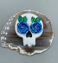 Load image into Gallery viewer, Cremation memorial art, such as Day of the Dead Spirit Pieces, provide a unique way to keep a loved one close to your heart. Handcrafted with care, each piece of artwork is specially tailored to the individual, providing a lasting reminder of those who are dearly missed. On altars and ofrendas, these pieces make a beautiful addition. Composed with meticulous attention to detail, these mini polymer clay skulls feature hand sculpted bright blue roses and leaves. H 1 1/2” x W 1 1/2” x D 3/4”