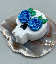 Load image into Gallery viewer, Cremation memorial art, such as Day of the Dead Spirit Pieces, provide a unique way to keep a loved one close to your heart. Handcrafted with care, each piece of artwork is specially tailored to the individual, providing a lasting reminder of those who are dearly missed. On altars and ofrendas, these pieces make a beautiful addition. Composed with meticulous attention to detail, these mini polymer clay skulls feature hand sculpted bright blue roses and leaves. H 1 1/2” x W 1 1/2” x D 3/4”