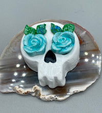 Load image into Gallery viewer, Cremation memorial art, such as Day of the Dead Spirit Pieces, provide a unique way to keep a loved one close to your heart. Handcrafted with care, each piece of artwork is specially tailored to the individual, providing a lasting reminder of those who are dearly missed. On altars and ofrendas, these pieces make a beautiful addition. Composed with meticulous attention to detail, these mini polymer clay skulls feature hand sculpted light blue roses and leaves. H 1 1/2” x W 1 1/2” x D 3/4”