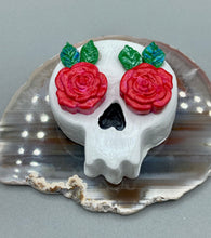Load image into Gallery viewer, Cremation memorial art, such as Day of the Dead Spirit Pieces, provide a unique way to keep a loved one close to your heart. Handcrafted with care, each piece of artwork is specially tailored to the individual, providing a lasting reminder of those who are dearly missed. On altars and ofrendas, these pieces make a beautiful addition. Composed with meticulous attention to detail, these mini polymer clay skulls feature hand sculpted bright pink roses and leaves. H 1 1/2” x W 1 1/2” x D 3/4”