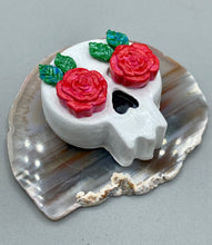 Load image into Gallery viewer, Cremation memorial art, such as Day of the Dead Spirit Pieces, provide a unique way to keep a loved one close to your heart. Handcrafted with care, each piece of artwork is specially tailored to the individual, providing a lasting reminder of those who are dearly missed. On altars and ofrendas, these pieces make a beautiful addition. Composed with meticulous attention to detail, these mini polymer clay skulls feature hand sculpted bright pink roses and leaves. H 1 1/2” x W 1 1/2” x D 3/4”