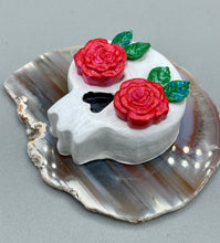 Load image into Gallery viewer, Cremation memorial art, such as Day of the Dead Spirit Pieces, provide a unique way to keep a loved one close to your heart. Handcrafted with care, each piece of artwork is specially tailored to the individual, providing a lasting reminder of those who are dearly missed. On altars and ofrendas, these pieces make a beautiful addition. Composed with meticulous attention to detail, these mini polymer clay skulls feature hand sculpted bright pink roses and leaves. H 1 1/2” x W 1 1/2” x D 3/4”