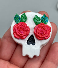 Load image into Gallery viewer, Cremation memorial art, such as Day of the Dead Spirit Pieces, provide a unique way to keep a loved one close to your heart. Handcrafted with care, each piece of artwork is specially tailored to the individual, providing a lasting reminder of those who are dearly missed. On altars and ofrendas, these pieces make a beautiful addition. Composed with meticulous attention to detail, these mini polymer clay skulls feature hand sculpted bright pink roses and leaves. H 1 1/2” x W 1 1/2” x D 3/4”