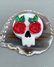 Load image into Gallery viewer, Cremation memorial art, such as Day of the Dead Spirit Pieces, provide a unique way to keep a loved one close to your heart. Handcrafted with care, each piece of artwork is specially tailored to the individual, providing a lasting reminder of those who are dearly missed. On altars and ofrendas, these pieces make a beautiful addition. Composed with meticulous attention to detail, these mini polymer clay skulls feature hand sculpted bright pink roses and leaves. H 1 1/2” x W 1 1/2” x D 3/4”