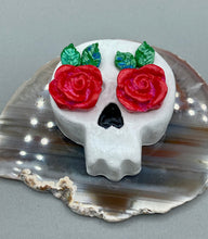 Load image into Gallery viewer, Cremation memorial art, such as Day of the Dead Spirit Pieces, provide a unique way to keep a loved one close to your heart. Handcrafted with care, each piece of artwork is specially tailored to the individual, providing a lasting reminder of those who are dearly missed. On altars and ofrendas, these pieces make a beautiful addition. Composed with meticulous attention to detail, these mini polymer clay skulls feature hand sculpted bright pink roses and leaves. H 1 1/2” x W 1 1/2” x D 3/4”