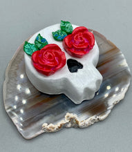 Load image into Gallery viewer, Cremation memorial art, such as Day of the Dead Spirit Pieces, provide a unique way to keep a loved one close to your heart. Handcrafted with care, each piece of artwork is specially tailored to the individual, providing a lasting reminder of those who are dearly missed. On altars and ofrendas, these pieces make a beautiful addition. Composed with meticulous attention to detail, these mini polymer clay skulls feature hand sculpted bright pink roses and leaves. H 1 1/2” x W 1 1/2” x D 3/4”