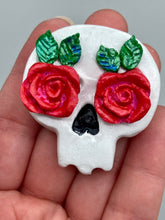 Load image into Gallery viewer, Cremation memorial art, such as Day of the Dead Spirit Pieces, provide a unique way to keep a loved one close to your heart. Handcrafted with care, each piece of artwork is specially tailored to the individual, providing a lasting reminder of those who are dearly missed. On altars and ofrendas, these pieces make a beautiful addition. Composed with meticulous attention to detail, these mini polymer clay skulls feature hand sculpted bright pink roses and leaves. H 1 1/2” x W 1 1/2” x D 3/4”