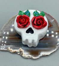 Load image into Gallery viewer, Cremation memorial art, such as Day of the Dead Spirit Pieces, provide a unique way to keep a loved one close to your heart. Handcrafted with care, each piece of artwork is specially tailored to the individual, providing a lasting reminder of those who are dearly missed. On altars and ofrendas, these pieces make a beautiful addition. Composed with meticulous attention to detail, these mini polymer clay skulls feature hand sculpted bright red roses and leaves. H 1 1/2” x W 1 1/2” x D 3/4”