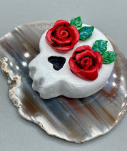 Load image into Gallery viewer, Cremation memorial art, such as Day of the Dead Spirit Pieces, provide a unique way to keep a loved one close to your heart. Handcrafted with care, each piece of artwork is specially tailored to the individual, providing a lasting reminder of those who are dearly missed. On altars and ofrendas, these pieces make a beautiful addition. Composed with meticulous attention to detail, these mini polymer clay skulls feature hand sculpted bright red roses and leaves. H 1 1/2” x W 1 1/2” x D 3/4”