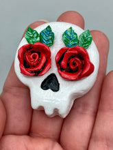 Load image into Gallery viewer, Cremation memorial art, such as Day of the Dead Spirit Pieces, provide a unique way to keep a loved one close to your heart. Handcrafted with care, each piece of artwork is specially tailored to the individual, providing a lasting reminder of those who are dearly missed. On altars and ofrendas, these pieces make a beautiful addition. Composed with meticulous attention to detail, these mini polymer clay skulls feature hand sculpted bright red roses and leaves. H 1 1/2” x W 1 1/2” x D 3/4”