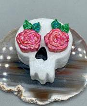 Load image into Gallery viewer, Cremation memorial art, such as Day of the Dead Spirit Pieces, provide a unique way to keep a loved one close to your heart. Handcrafted with care, each piece of artwork is specially tailored to the individual, providing a lasting reminder of those who are dearly missed. On altars and ofrendas, these pieces make a beautiful addition. Composed with meticulous attention to detail, these mini polymer clay skulls feature hand sculpted light pink roses and leaves. H 1 1/2” x W 1 1/2” x D 3/4”