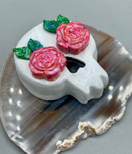 Load image into Gallery viewer, Cremation memorial art, such as Day of the Dead Spirit Pieces, provide a unique way to keep a loved one close to your heart. Handcrafted with care, each piece of artwork is specially tailored to the individual, providing a lasting reminder of those who are dearly missed. On altars and ofrendas, these pieces make a beautiful addition. Composed with meticulous attention to detail, these mini polymer clay skulls feature hand sculpted light pink roses and leaves. H 1 1/2” x W 1 1/2” x D 3/4”