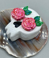 Load image into Gallery viewer, Cremation memorial art, such as Day of the Dead Spirit Pieces, provide a unique way to keep a loved one close to your heart. Handcrafted with care, each piece of artwork is specially tailored to the individual, providing a lasting reminder of those who are dearly missed. On altars and ofrendas, these pieces make a beautiful addition. Composed with meticulous attention to detail, these mini polymer clay skulls feature hand sculpted light pink roses and leaves. H 1 1/2” x W 1 1/2” x D 3/4”
