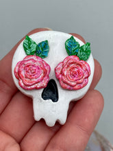 Load image into Gallery viewer, Cremation memorial art, such as Day of the Dead Spirit Pieces, provide a unique way to keep a loved one close to your heart. Handcrafted with care, each piece of artwork is specially tailored to the individual, providing a lasting reminder of those who are dearly missed. On altars and ofrendas, these pieces make a beautiful addition. Composed with meticulous attention to detail, these mini polymer clay skulls feature hand sculpted light pink roses and leaves. H 1 1/2” x W 1 1/2” x D 3/4”