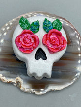 Load image into Gallery viewer, Cremation memorial art, such as Day of the Dead Spirit Pieces, provide a unique way to keep a loved one close to your heart. Handcrafted with care, each piece of artwork is specially tailored to the individual, providing a lasting reminder of those who are dearly missed. On altars and ofrendas, these pieces make a beautiful addition. Composed with meticulous attention to detail, these mini polymer clay skulls feature hand sculpted pink roses and leaves. H 1 1/2” x W 1 1/2” x D 3/4”