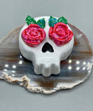 Load image into Gallery viewer, Cremation memorial art, such as Day of the Dead Spirit Pieces, provide a unique way to keep a loved one close to your heart. Handcrafted with care, each piece of artwork is specially tailored to the individual, providing a lasting reminder of those who are dearly missed. On altars and ofrendas, these pieces make a beautiful addition. Composed with meticulous attention to detail, these mini polymer clay skulls feature hand sculpted pink roses and leaves. H 1 1/2” x W 1 1/2” x D 3/4”