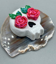 Load image into Gallery viewer, Cremation memorial art, such as Day of the Dead Spirit Pieces, provide a unique way to keep a loved one close to your heart. Handcrafted with care, each piece of artwork is specially tailored to the individual, providing a lasting reminder of those who are dearly missed. On altars and ofrendas, these pieces make a beautiful addition. Composed with meticulous attention to detail, these mini polymer clay skulls feature hand sculpted pink roses and leaves. H 1 1/2” x W 1 1/2” x D 3/4”
