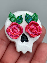 Load image into Gallery viewer, Cremation memorial art, such as Day of the Dead Spirit Pieces, provide a unique way to keep a loved one close to your heart. Handcrafted with care, each piece of artwork is specially tailored to the individual, providing a lasting reminder of those who are dearly missed. On altars and ofrendas, these pieces make a beautiful addition. Composed with meticulous attention to detail, these mini polymer clay skulls feature hand sculpted pink roses and leaves. H 1 1/2” x W 1 1/2” x D 3/4”