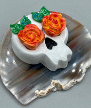 Load image into Gallery viewer, Cremation memorial art, such as Day of the Dead Spirit Pieces, provide a unique way to keep a loved one close to your heart. Handcrafted with care, each piece of artwork is specially tailored to the individual, providing a lasting reminder of those who are dearly missed. On altars and ofrendas, these pieces make a beautiful addition. Composed with meticulous attention to detail, these mini polymer clay skulls feature hand sculpted bright orange/yellow roses and leaves. H 1 1/2” x W 1 1/2” x D 3/4”