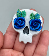 Load image into Gallery viewer, Cremation memorial art, such as Day of the Dead Spirit Pieces, provide a unique way to keep a loved one close to your heart. Handcrafted with care, each piece of artwork is specially tailored to the individual, providing a lasting reminder of those who are dearly missed. On altars and ofrendas, these pieces make a beautiful addition. Composed with meticulous attention to detail, these mini polymer clay skulls feature hand sculpted dark blue roses and leaves. H 1 1/2” x W 1 1/2” x D 3/4”