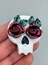 Load image into Gallery viewer, Cremation memorial art, such as Day of the Dead Spirit Pieces, provide a unique way to keep a loved one close to your heart. Handcrafted with care, each piece of artwork is specially tailored to the individual, providing a lasting reminder of those who are dearly missed. On altars and ofrendas, these pieces make a beautiful addition. Composed with meticulous attention to detail, these mini polymer clay skulls feature hand sculpted dark red roses and leaves. H 1 1/2” x W 1 1/2” x D 3/4”