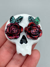 Load image into Gallery viewer, Cremation memorial art, such as Day of the Dead Spirit Pieces, provide a unique way to keep a loved one close to your heart. Handcrafted with care, each piece of artwork is specially tailored to the individual, providing a lasting reminder of those who are dearly missed. On altars and ofrendas, these pieces make a beautiful addition. Composed with meticulous attention to detail, these mini polymer clay skulls feature hand sculpted dark red roses and leaves. H 1 1/2” x W 1 1/2” x D 3/4”