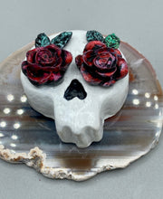 Load image into Gallery viewer, Cremation memorial art, such as Day of the Dead Spirit Pieces, provide a unique way to keep a loved one close to your heart. Handcrafted with care, each piece of artwork is specially tailored to the individual, providing a lasting reminder of those who are dearly missed. On altars and ofrendas, these pieces make a beautiful addition. Composed with meticulous attention to detail, these mini polymer clay skulls feature hand sculpted dark red roses and leaves. H 1 1/2” x W 1 1/2” x D 3/4”
