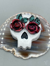 Load image into Gallery viewer, Cremation memorial art, such as Day of the Dead Spirit Pieces, provide a unique way to keep a loved one close to your heart. Handcrafted with care, each piece of artwork is specially tailored to the individual, providing a lasting reminder of those who are dearly missed. On altars and ofrendas, these pieces make a beautiful addition. Composed with meticulous attention to detail, these mini polymer clay skulls feature hand sculpted dark red roses and leaves. H 1 1/2” x W 1 1/2” x D 3/4”